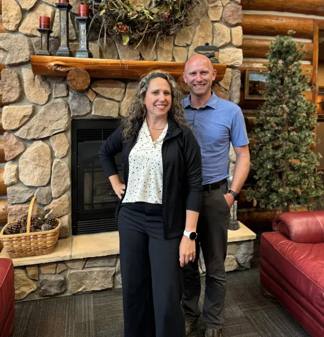 Amanda and Jeremy Mavis standing together beside a stone fireplace